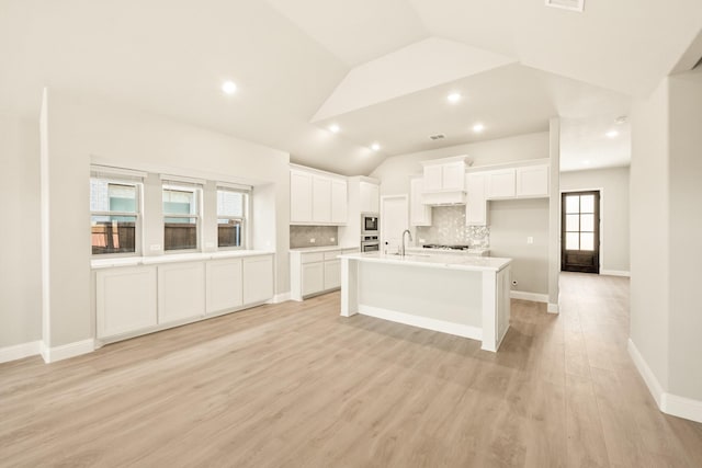 kitchen with light wood-style flooring, vaulted ceiling, white cabinets, and backsplash