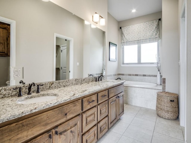 bathroom with a relaxing tiled tub, vanity, and tile patterned flooring