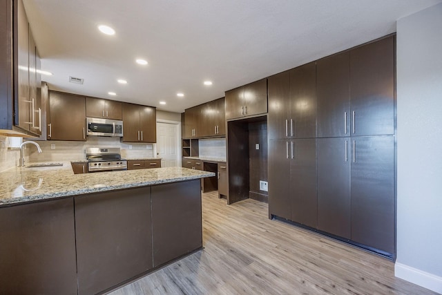 kitchen with sink, light stone countertops, light wood-type flooring, kitchen peninsula, and stainless steel appliances