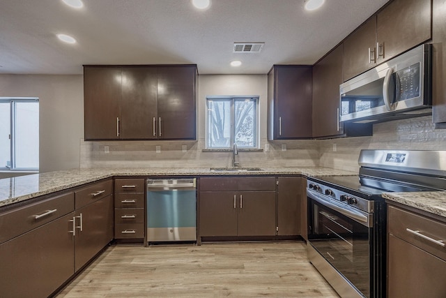 kitchen featuring light stone countertops, appliances with stainless steel finishes, light hardwood / wood-style floors, and sink