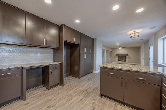 kitchen featuring backsplash, ceiling fan, light wood-type flooring, light stone countertops, and dark brown cabinets