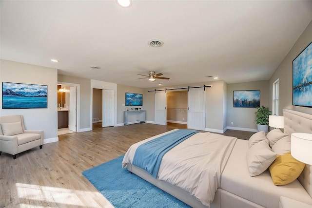 bedroom with ceiling fan, a barn door, light hardwood / wood-style flooring, and ensuite bath