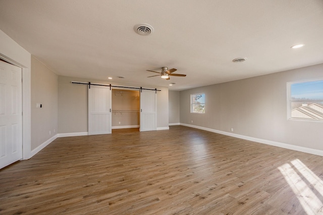 unfurnished bedroom featuring a barn door, ceiling fan, and wood-type flooring