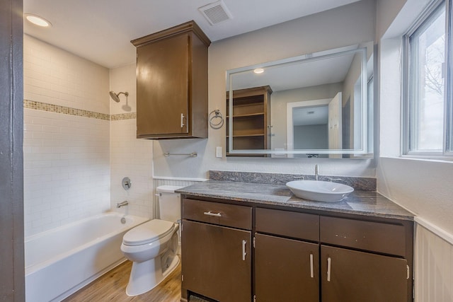 full bathroom featuring plenty of natural light, wood-type flooring, toilet, vanity, and tiled shower / bath