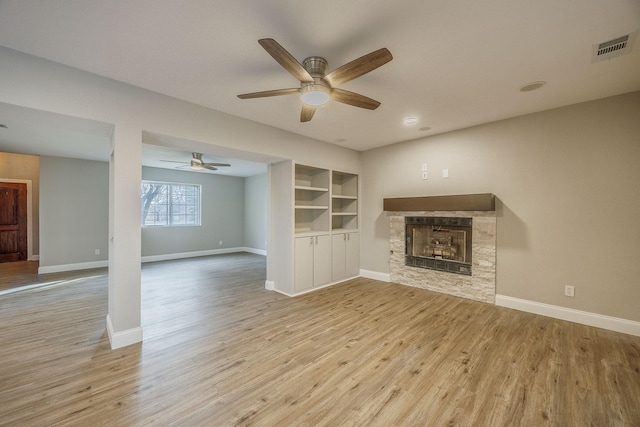 unfurnished living room with a stone fireplace, ceiling fan, built in features, and light hardwood / wood-style flooring