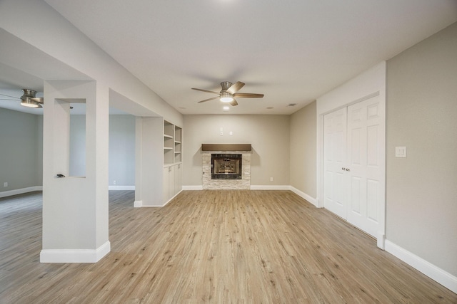 unfurnished living room featuring a fireplace, ceiling fan, built in features, and light hardwood / wood-style flooring