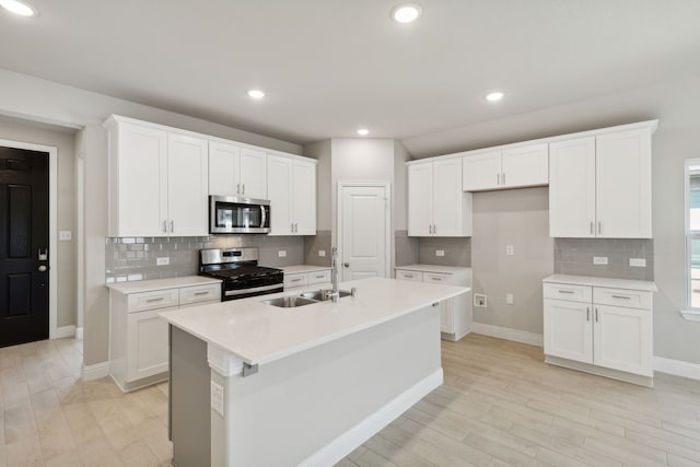 kitchen featuring sink, light hardwood / wood-style flooring, appliances with stainless steel finishes, an island with sink, and white cabinets