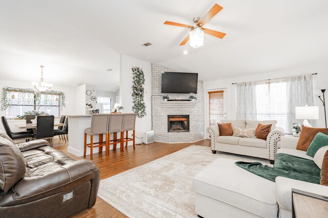 living room featuring a fireplace, light hardwood / wood-style flooring, ceiling fan with notable chandelier, and lofted ceiling