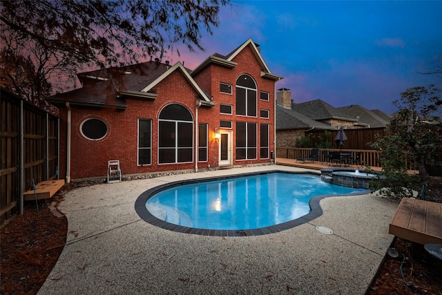 pool at dusk with a patio area and an in ground hot tub