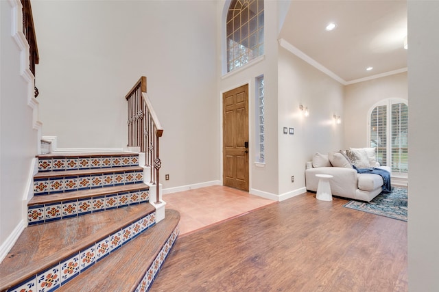 entrance foyer with wood-type flooring, a high ceiling, and ornamental molding