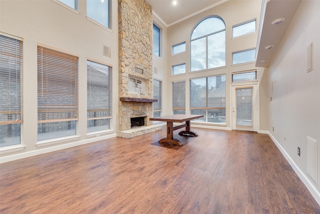 unfurnished living room with a fireplace, wood-type flooring, a towering ceiling, and ornamental molding