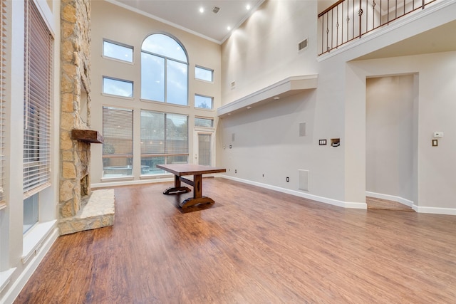 interior space with a stone fireplace, crown molding, a high ceiling, and hardwood / wood-style flooring