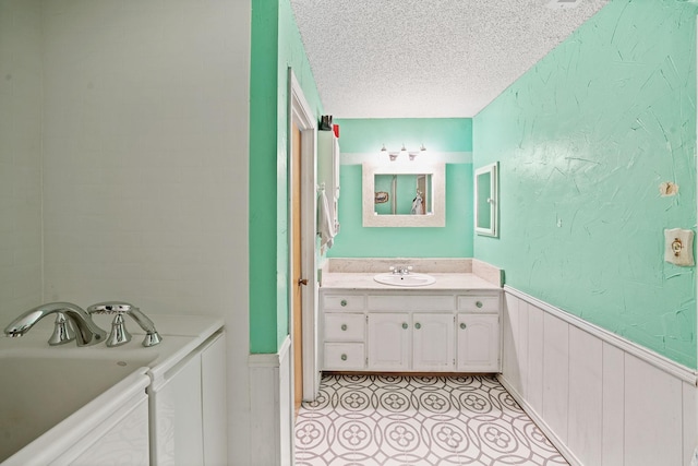 bathroom featuring a textured ceiling, a textured wall, a garden tub, vanity, and wainscoting