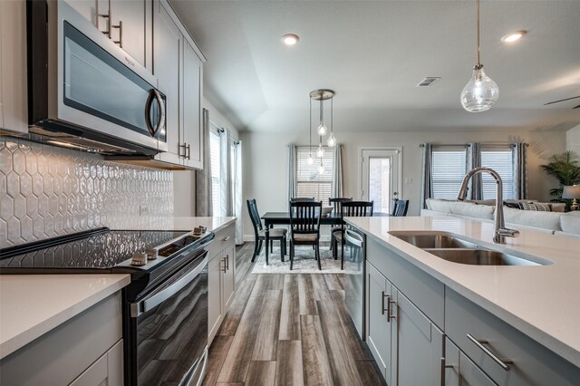 kitchen featuring pendant lighting, appliances with stainless steel finishes, wood-type flooring, sink, and gray cabinets