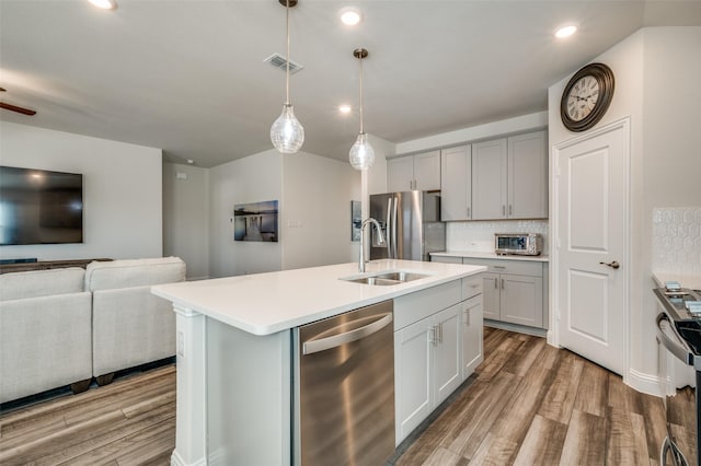 kitchen with hanging light fixtures, appliances with stainless steel finishes, sink, tasteful backsplash, and a center island with sink