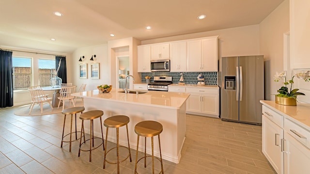 kitchen featuring a breakfast bar, an island with sink, white cabinetry, sink, and stainless steel appliances