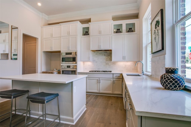 kitchen featuring decorative backsplash, stainless steel double oven, sink, white cabinets, and a center island