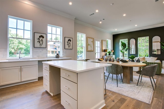 kitchen with a center island, sink, crown molding, white cabinets, and light wood-type flooring