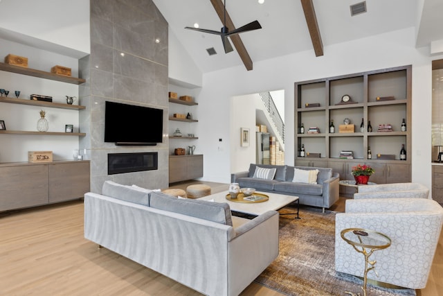 living room featuring high vaulted ceiling, ceiling fan, a high end fireplace, beam ceiling, and light hardwood / wood-style flooring