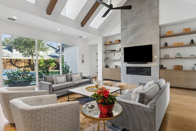 living room featuring a fireplace, a skylight, beamed ceiling, ceiling fan, and light wood-type flooring