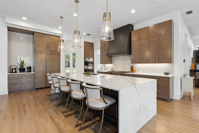 kitchen featuring pendant lighting, a breakfast bar, a spacious island, wall chimney exhaust hood, and light wood-type flooring