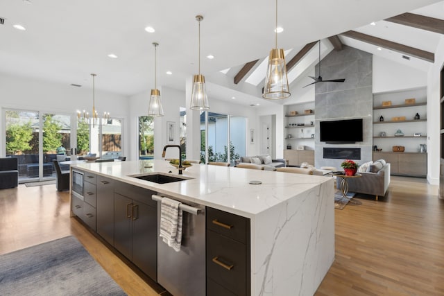 kitchen with sink, light stone counters, decorative light fixtures, stainless steel dishwasher, and a large island with sink