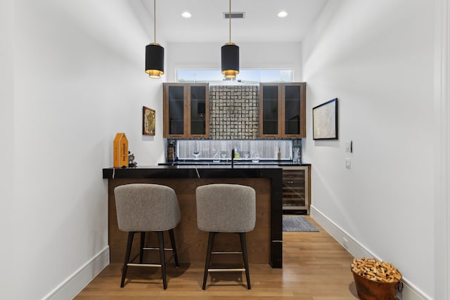 bar featuring decorative light fixtures, tasteful backsplash, sink, wine cooler, and light wood-type flooring