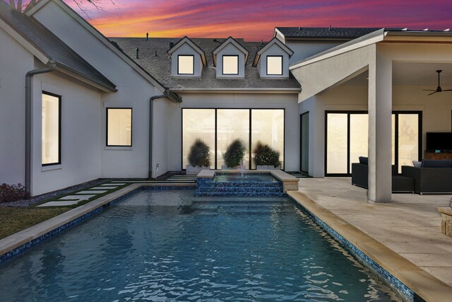 back house at dusk featuring ceiling fan, a pool with hot tub, an outdoor living space, and a patio