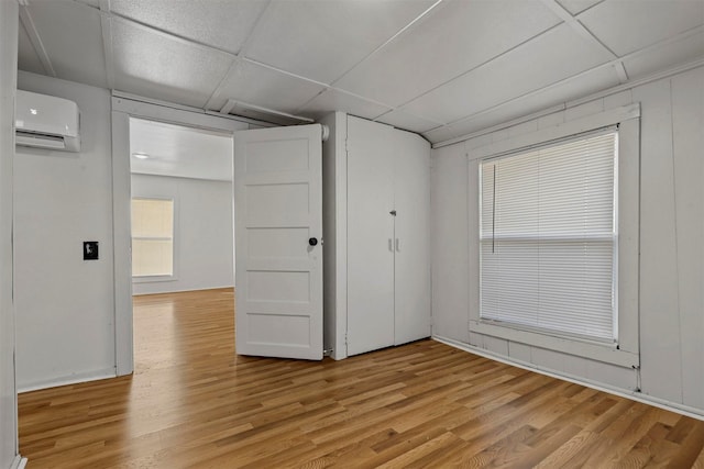 unfurnished room featuring a wall mounted air conditioner, light wood-type flooring, and a paneled ceiling