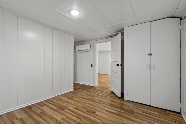 unfurnished bedroom with a paneled ceiling, light hardwood / wood-style flooring, and an AC wall unit