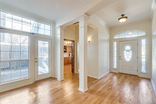 foyer entrance featuring a healthy amount of sunlight, light wood-type flooring, ornamental molding, and decorative columns