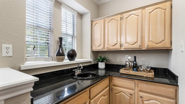 kitchen with a wealth of natural light, light brown cabinetry, dark stone counters, and sink