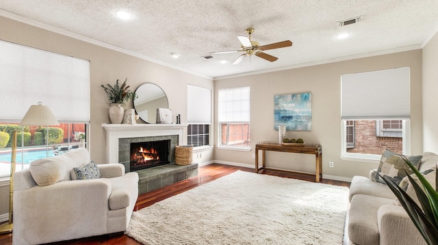 living room with ceiling fan, a tiled fireplace, dark hardwood / wood-style floors, and a textured ceiling