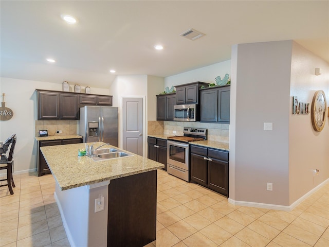 kitchen featuring sink, stainless steel appliances, tasteful backsplash, and an island with sink