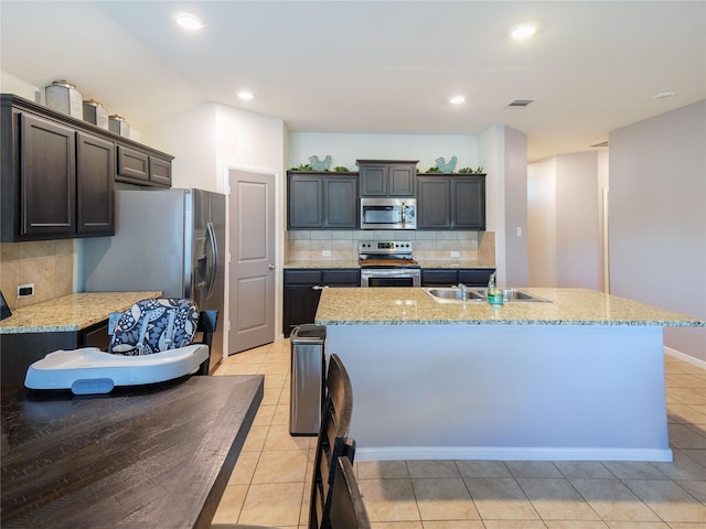 kitchen with decorative backsplash, stainless steel appliances, a kitchen island with sink, sink, and light tile patterned floors