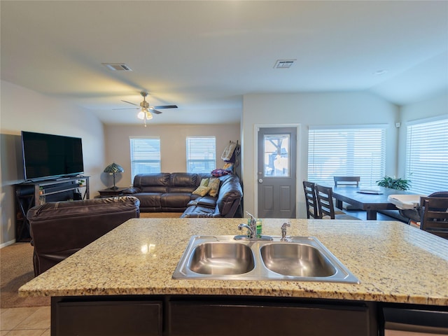 kitchen with a center island with sink, sink, ceiling fan, light tile patterned floors, and light stone counters