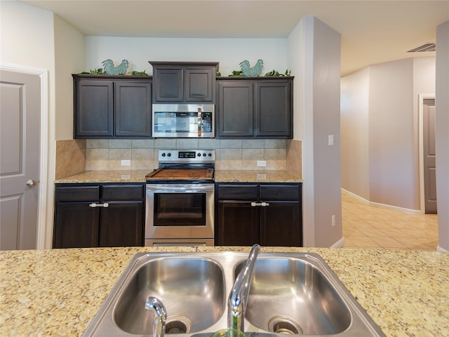 kitchen featuring backsplash, light stone counters, stainless steel appliances, sink, and light tile patterned floors