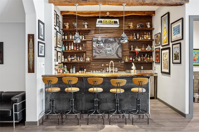 bar featuring pendant lighting, sink, hardwood / wood-style floors, wooden walls, and beamed ceiling