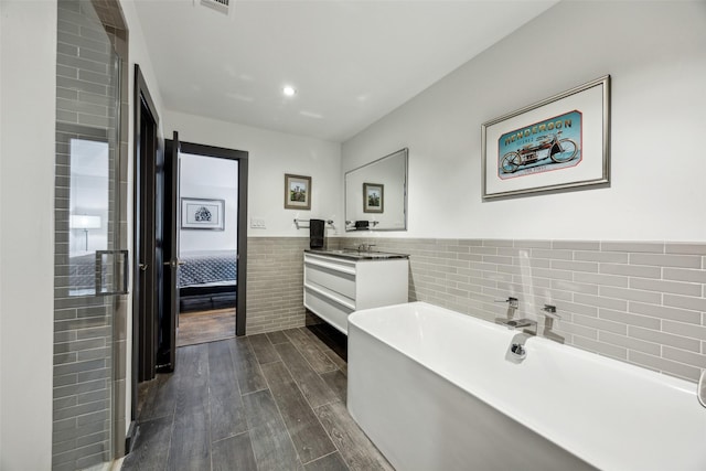 bathroom with hardwood / wood-style flooring, a tub to relax in, vanity, and tile walls