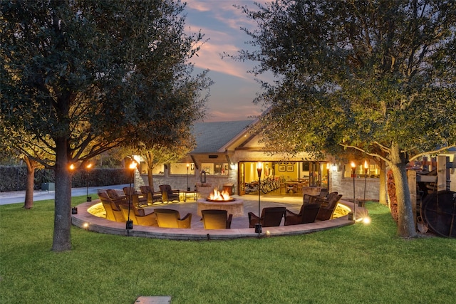 back house at dusk featuring a lawn, a patio area, and an outdoor fire pit