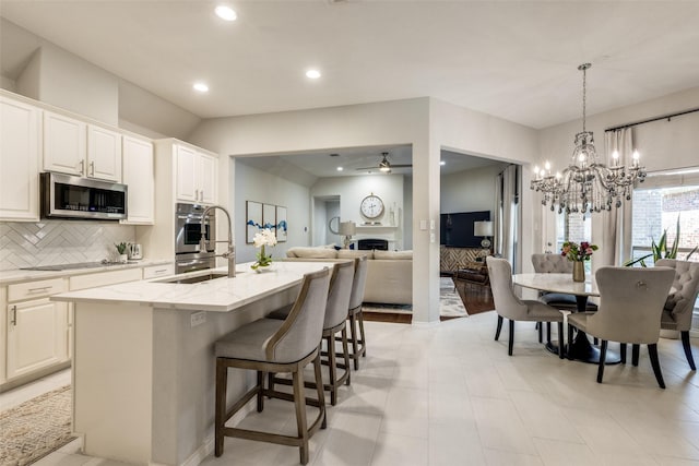 kitchen with white cabinetry, light stone countertops, tasteful backsplash, a center island with sink, and appliances with stainless steel finishes