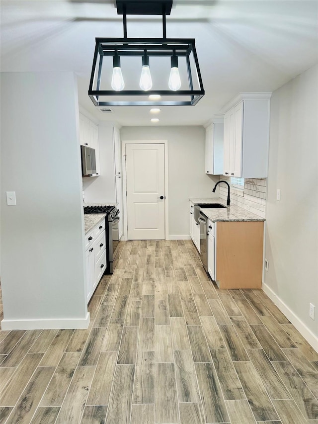 kitchen featuring appliances with stainless steel finishes, backsplash, white cabinets, light stone counters, and sink