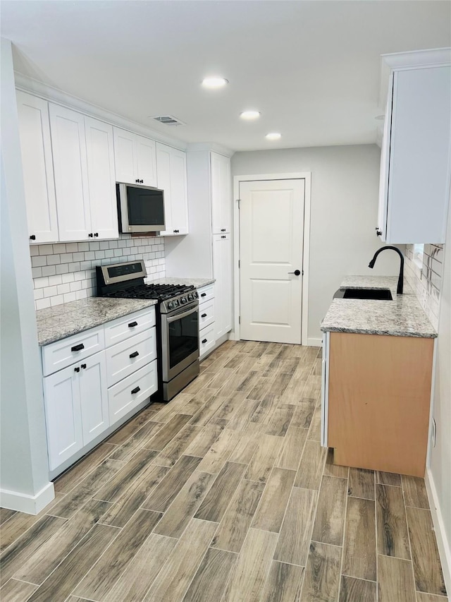 kitchen featuring sink, light stone counters, stainless steel appliances, and white cabinetry