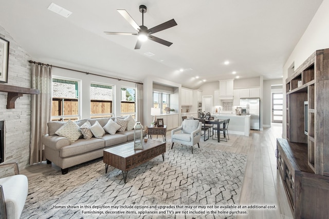 living room featuring ceiling fan, a stone fireplace, lofted ceiling, and light wood-type flooring