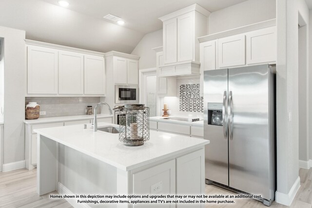 kitchen featuring white cabinetry, built in microwave, sink, stainless steel fridge, and a center island with sink