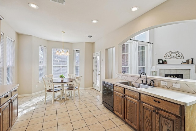 kitchen featuring sink, an inviting chandelier, black dishwasher, pendant lighting, and a fireplace