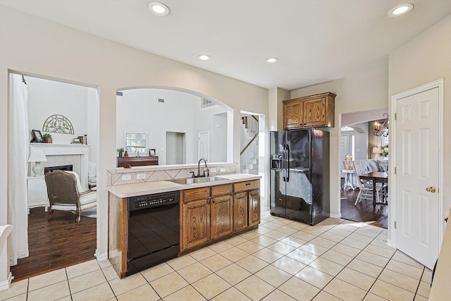 kitchen with a tile fireplace, sink, light tile patterned floors, and black appliances