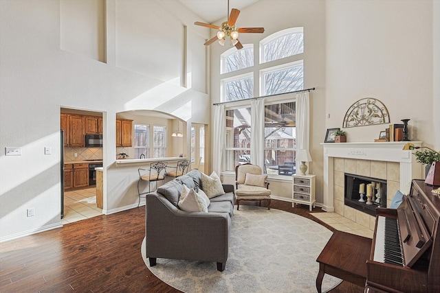 living room with ceiling fan, light hardwood / wood-style floors, a fireplace, and a high ceiling