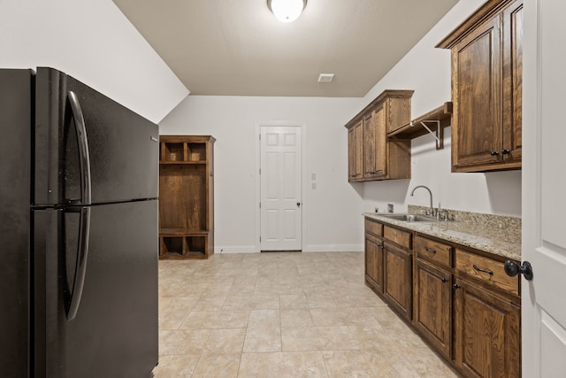 kitchen featuring light stone counters, sink, vaulted ceiling, and black fridge