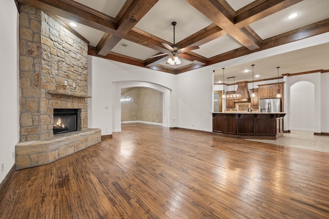 unfurnished living room featuring coffered ceiling, beamed ceiling, ceiling fan, a fireplace, and light hardwood / wood-style floors